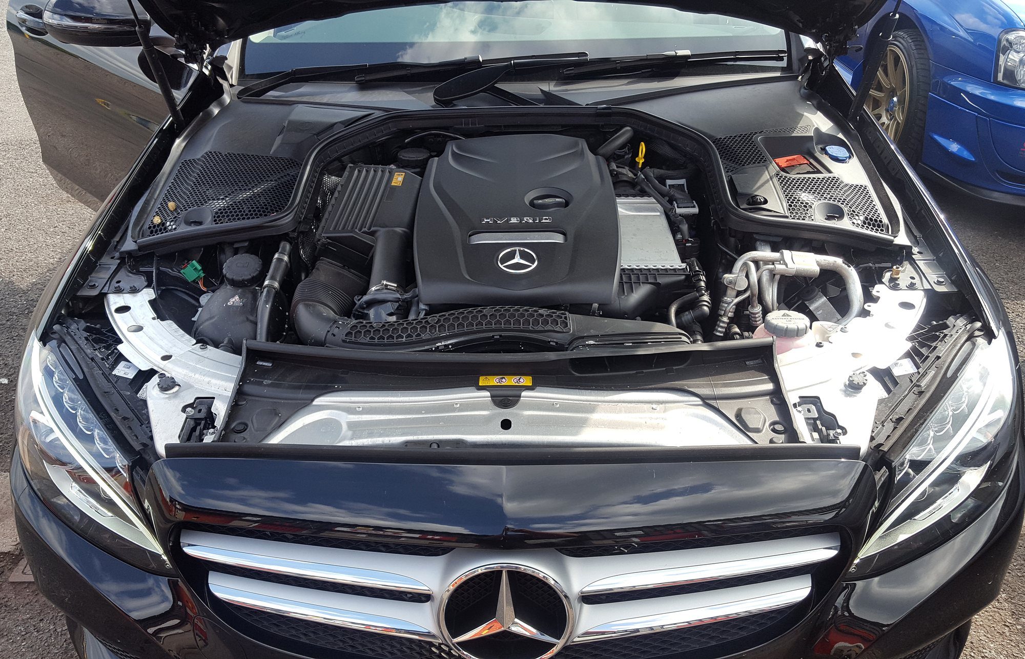A Mercedes-Benz C-Class hybrid with its bonnet up, a blue Subaru Impreza STI parked beside it